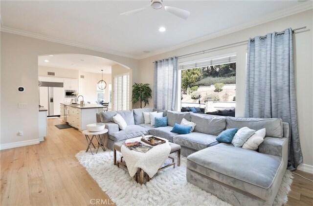 living room featuring baseboards, arched walkways, ornamental molding, and light wood-type flooring