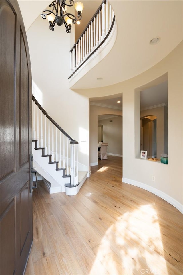 foyer with baseboards, arched walkways, a chandelier, and light wood-type flooring