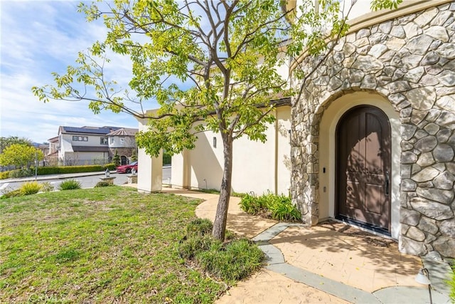 property entrance with a yard, stone siding, and stucco siding