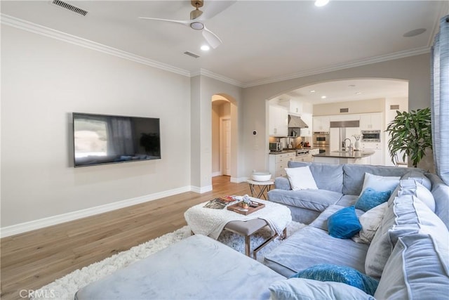 living area with baseboards, a ceiling fan, light wood-style floors, visible vents, and arched walkways
