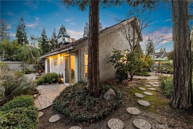 property exterior at dusk with a patio area, fence, and stucco siding