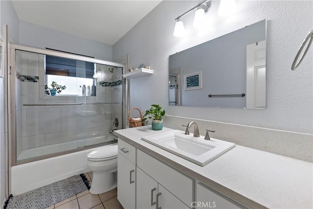 bathroom with a textured wall, toilet, bath / shower combo with glass door, vanity, and tile patterned floors