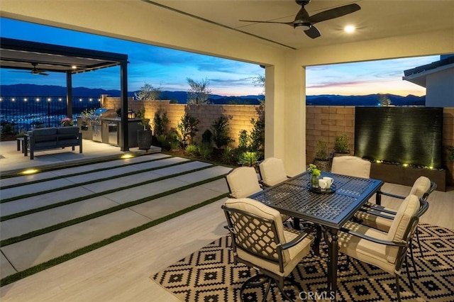 view of patio featuring ceiling fan, fence, outdoor dining area, and exterior kitchen