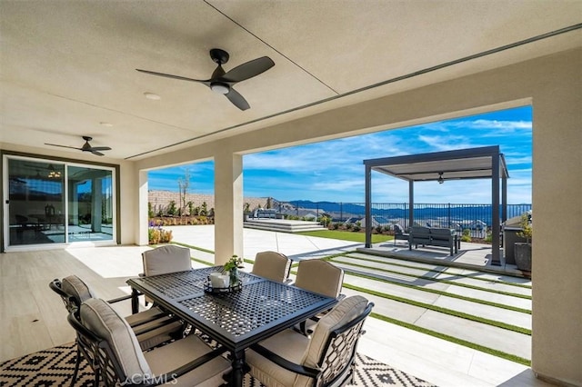 view of patio with ceiling fan, fence, a mountain view, and outdoor dining space