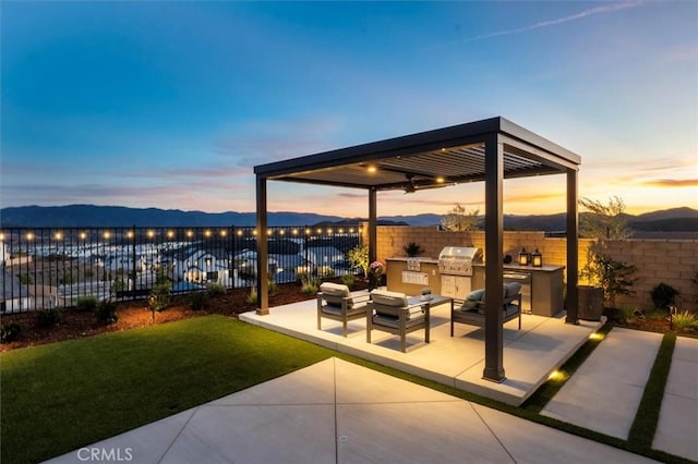 patio terrace at dusk with a yard, fence, and an outdoor kitchen