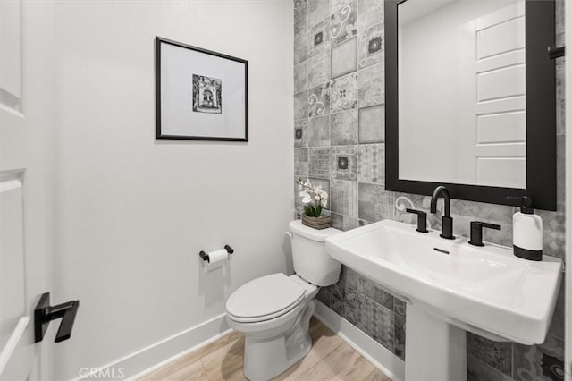 half bath featuring baseboards, wood finished floors, toilet, and tile walls