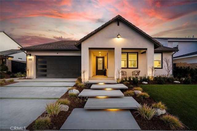 view of front of home with a porch, an attached garage, driveway, a lawn, and stucco siding