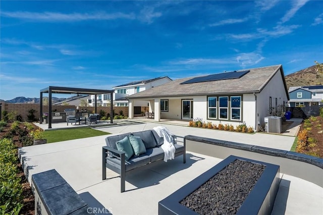 rear view of property with a fenced backyard, an outdoor hangout area, a patio area, roof mounted solar panels, and central AC