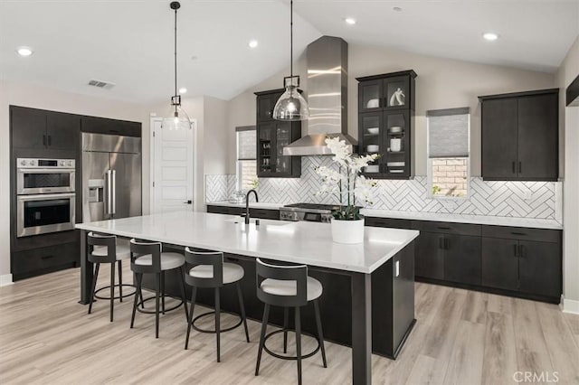 kitchen with visible vents, wall chimney exhaust hood, appliances with stainless steel finishes, light countertops, and a sink