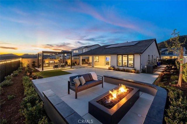 back of property at dusk with a patio, a fenced backyard, solar panels, stucco siding, and an outdoor living space with a fire pit