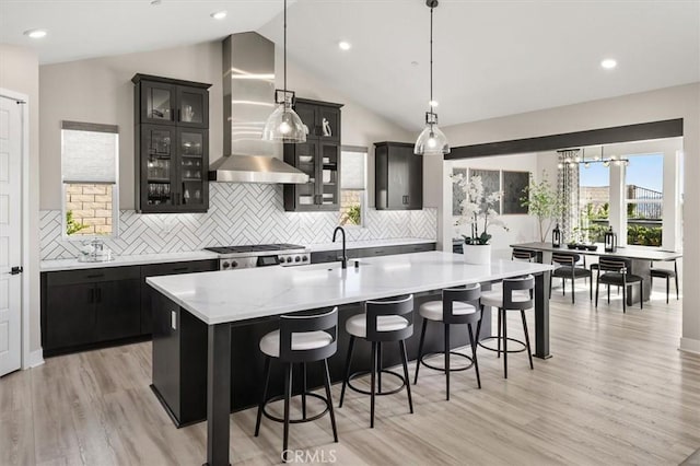 kitchen with dark cabinets, light wood-style floors, an island with sink, and extractor fan