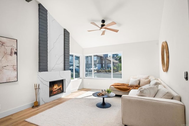 living room with lofted ceiling, ceiling fan, a premium fireplace, baseboards, and light wood-style floors