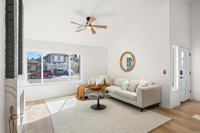 living area with high vaulted ceiling, light wood-style flooring, baseboards, and a ceiling fan