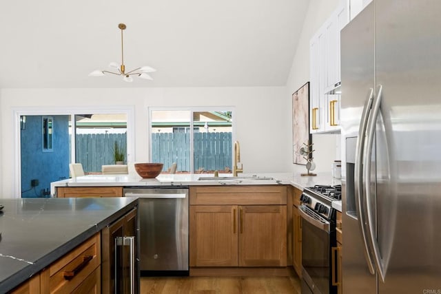 kitchen with lofted ceiling, appliances with stainless steel finishes, brown cabinets, and a sink