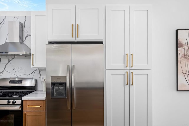 kitchen featuring light stone counters, appliances with stainless steel finishes, wall chimney range hood, and white cabinetry