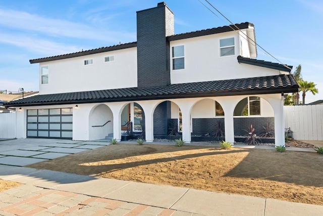 view of front of house featuring driveway, a chimney, a tiled roof, fence, and stucco siding