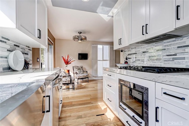 kitchen featuring light stone counters, light wood-type flooring, black appliances, white cabinetry, and backsplash