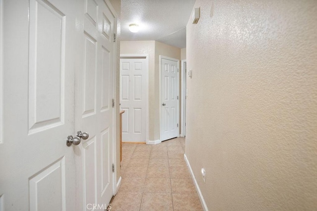 corridor featuring light tile patterned flooring, a textured wall, a textured ceiling, and baseboards