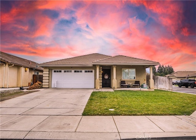 view of front facade with concrete driveway, an attached garage, fence, a yard, and stucco siding