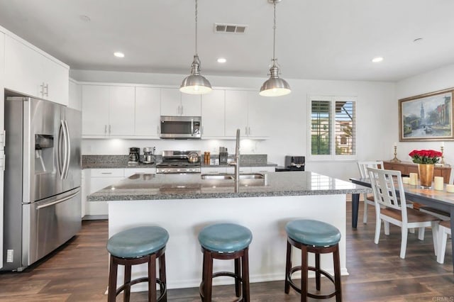 kitchen with pendant lighting, stainless steel appliances, visible vents, white cabinetry, and a sink