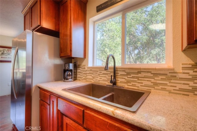 kitchen featuring tasteful backsplash, a sink, freestanding refrigerator, and light stone countertops