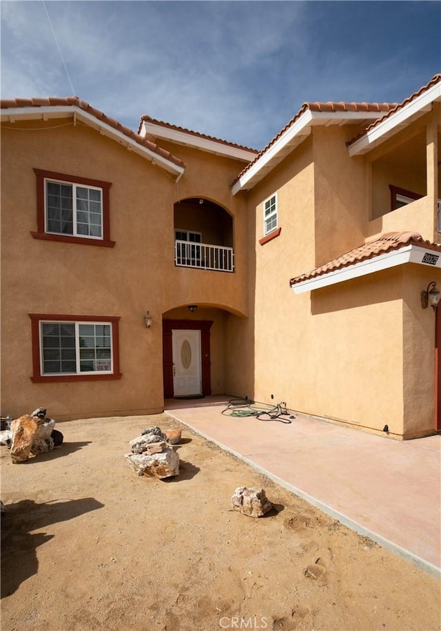 rear view of house featuring a patio, a tiled roof, and stucco siding