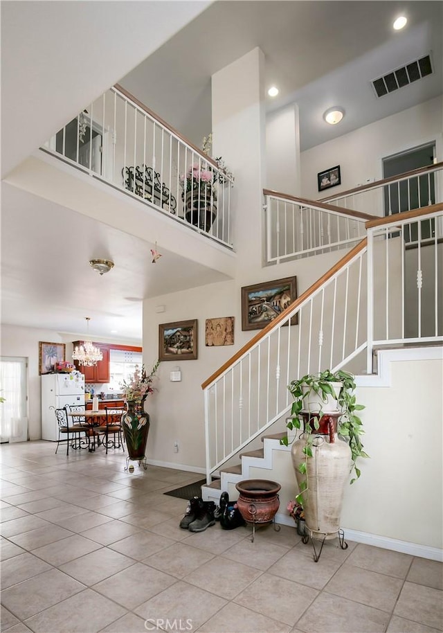 stairway featuring a notable chandelier, visible vents, a high ceiling, baseboards, and tile patterned floors