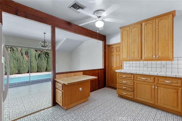 kitchen featuring beam ceiling, tile countertops, visible vents, wainscoting, and ceiling fan with notable chandelier