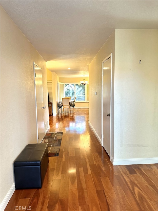 hallway featuring a chandelier, wood finished floors, and baseboards