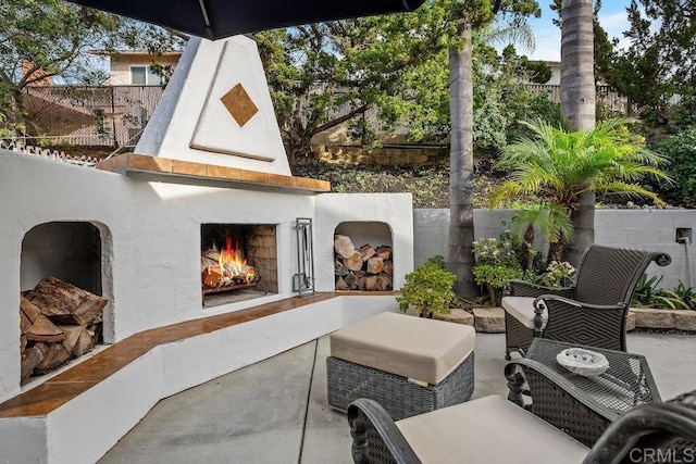 view of patio / terrace featuring a warm lit fireplace, fence, and grilling area