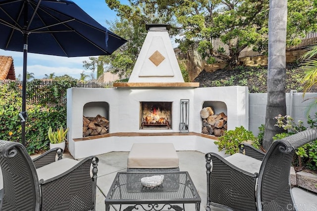 view of patio featuring a lit fireplace and fence