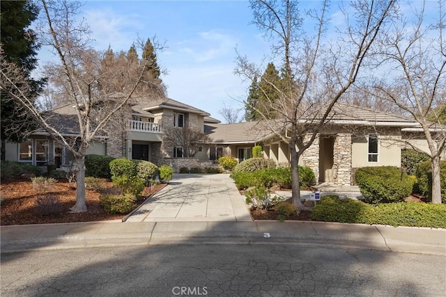 view of front of house with stone siding, a balcony, concrete driveway, and stucco siding