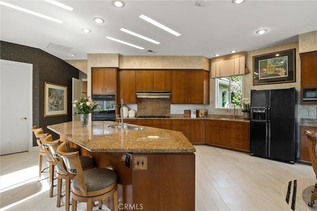 kitchen with brown cabinets, a sink, under cabinet range hood, black appliances, and wallpapered walls