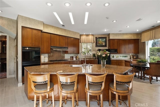 kitchen with a skylight, tasteful backsplash, a center island with sink, under cabinet range hood, and a sink