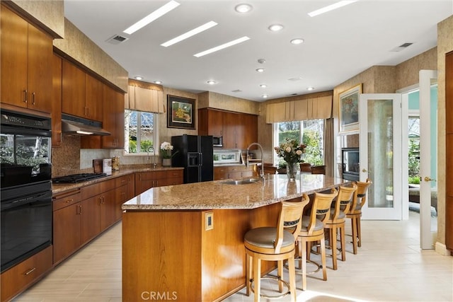 kitchen featuring plenty of natural light, a sink, under cabinet range hood, and black appliances