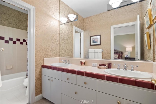 full bathroom featuring toilet, wallpapered walls, double vanity, and a sink