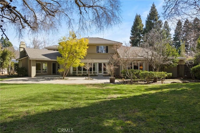 rear view of property featuring a patio area, a chimney, a lawn, and stucco siding