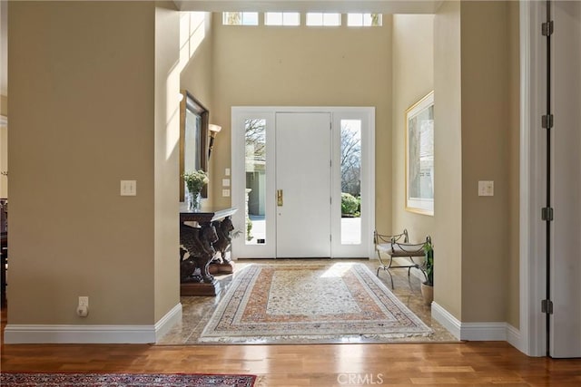 entrance foyer with wood finished floors, a towering ceiling, and baseboards