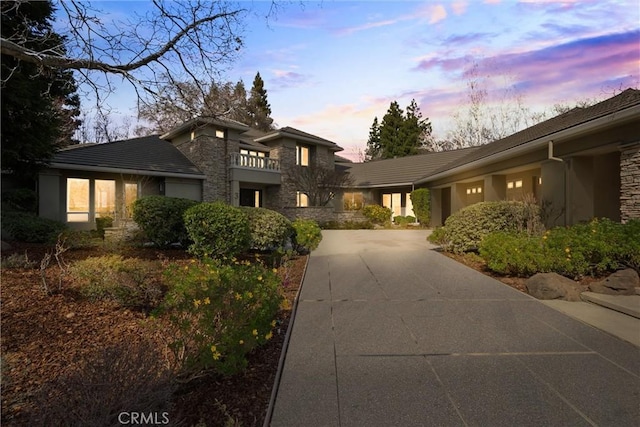 prairie-style house featuring a balcony, stone siding, concrete driveway, and stucco siding