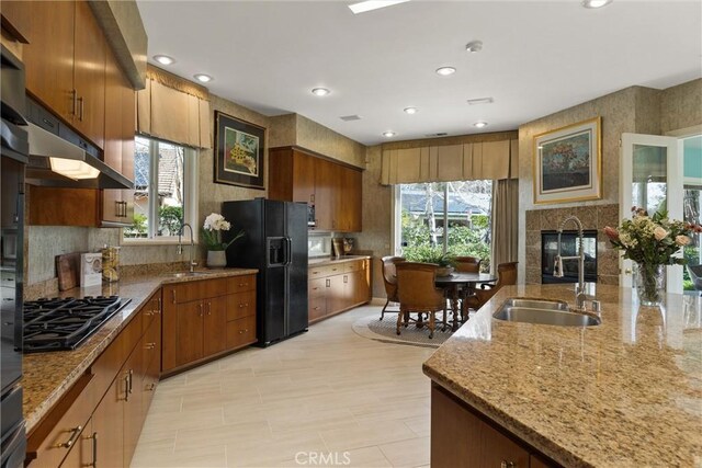 kitchen featuring a wealth of natural light, a tile fireplace, a sink, and black appliances