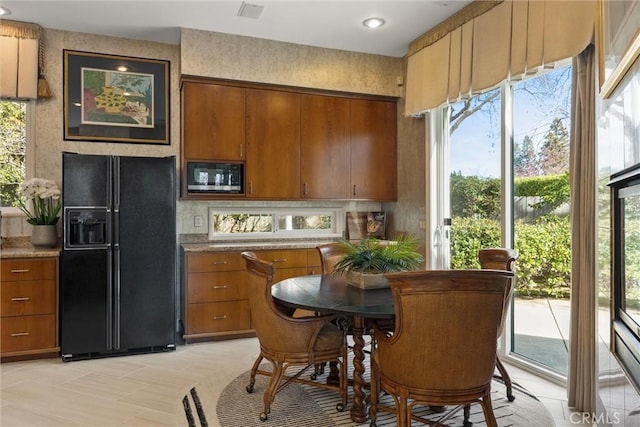 kitchen with built in microwave, visible vents, backsplash, brown cabinets, and black refrigerator with ice dispenser