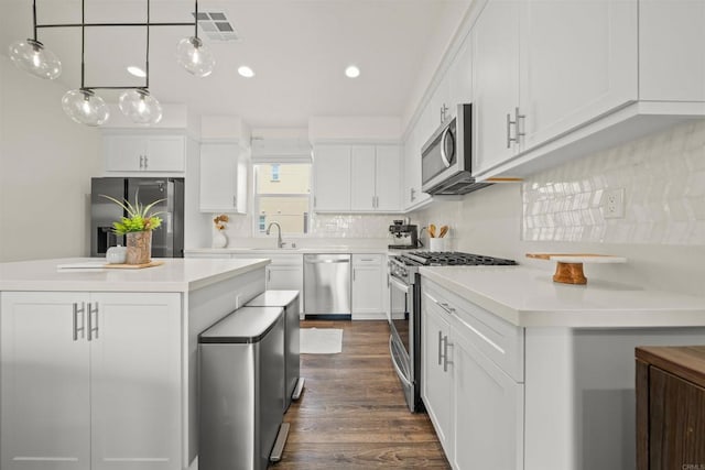 kitchen featuring white cabinets, a center island, hanging light fixtures, stainless steel appliances, and light countertops