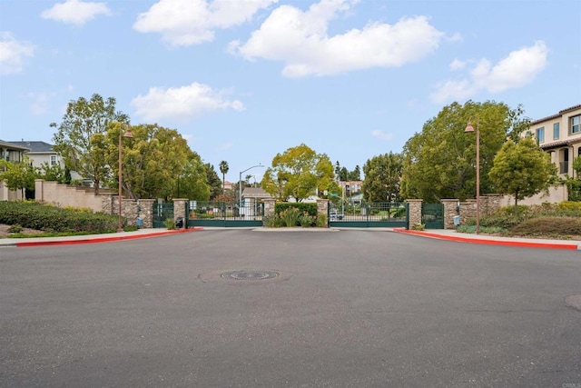 view of street featuring a gate, curbs, a gated entry, and street lights