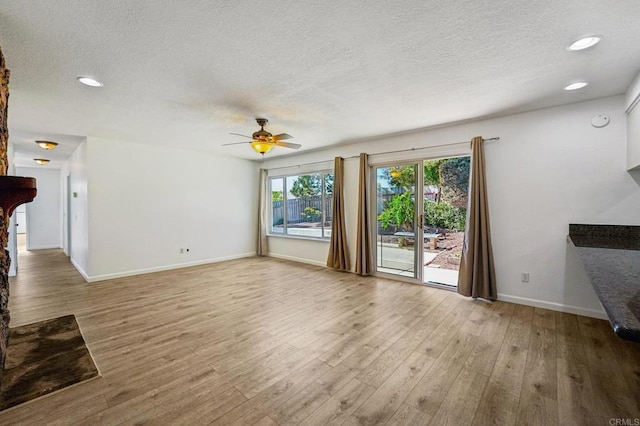 unfurnished living room with a textured ceiling, recessed lighting, light wood-type flooring, and baseboards