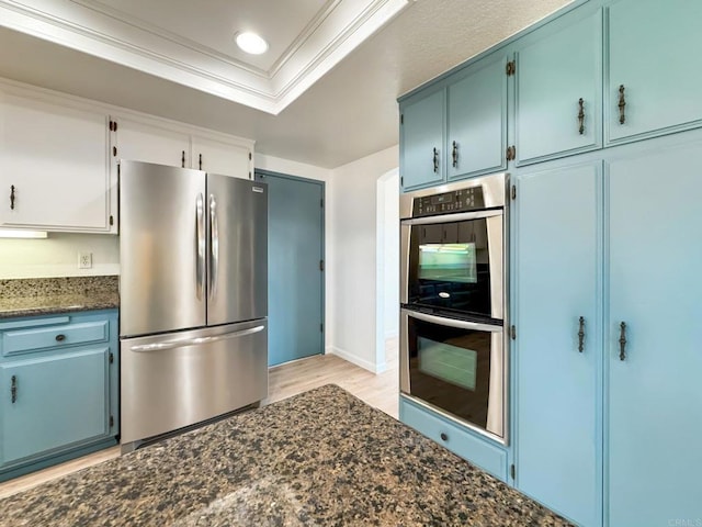 kitchen with white cabinets, ornamental molding, appliances with stainless steel finishes, dark stone countertops, and a raised ceiling