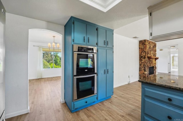 kitchen featuring dark stone countertops, blue cabinets, light wood-style floors, double oven, and a fireplace