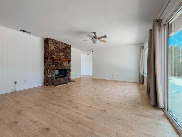 unfurnished living room featuring ceiling fan, a stone fireplace, visible vents, baseboards, and light wood finished floors