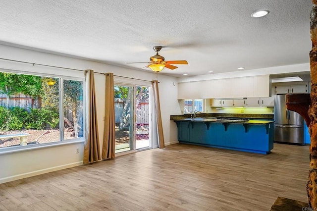 kitchen featuring dark countertops, freestanding refrigerator, a peninsula, white cabinetry, and a sink