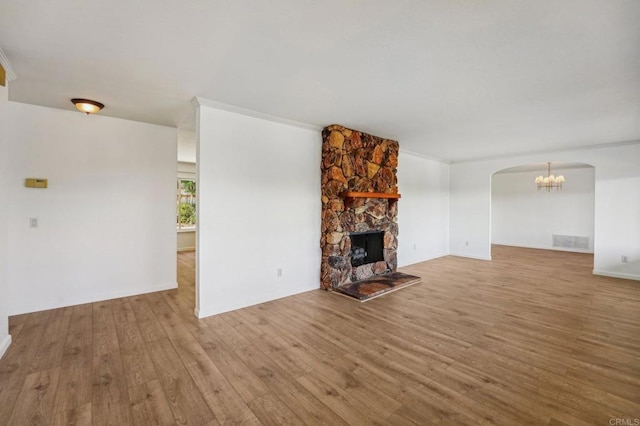 unfurnished living room featuring light wood-type flooring, a fireplace, visible vents, and arched walkways