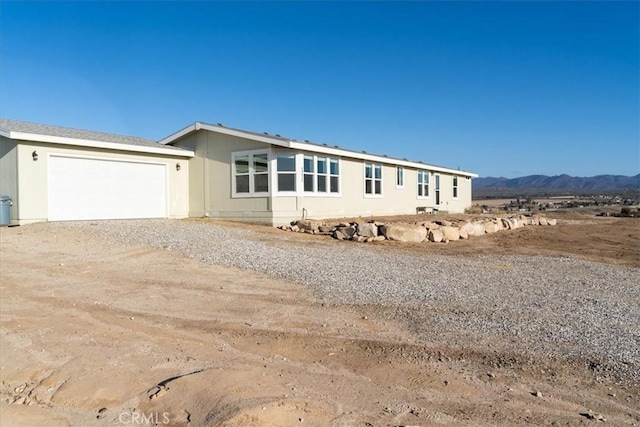 manufactured / mobile home with gravel driveway, a mountain view, and an attached garage